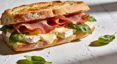 Brie peynirli lezzetli sandviç ve beyaz desenli masada jambon.