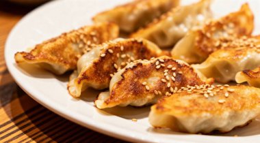 Tahta masada beyaz tabakta servis edilen susam tohumlu lezzetli kızarmış gyoza köfteleri.