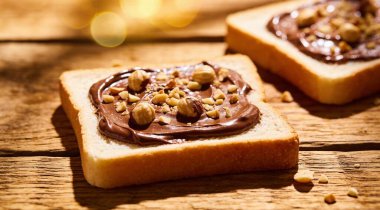 Çikolata sürülmüş ekmek dilimleri ve ahşap masada fındıklar.