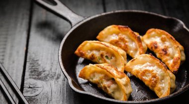 Kızarmış yaki Gyoza, siyah arka planda dökme demir tavada servis ediliyor.