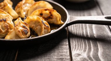 Kızarmış yaki Gyoza, siyah arka planda dökme demir tavada servis ediliyor.