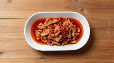 Kızarmış kırmızı biberli domuz etini ahşap masada beyaz tabakta karıştır.