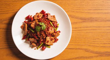 Kızarmış kırmızı biberli domuz etini ahşap masada beyaz tabakta karıştır.