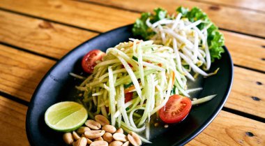 Tahta bir masada siyah tabakta yeşil papaya salatası, üst manzara. Tayland yemeklerinin en üst görüntüsü.