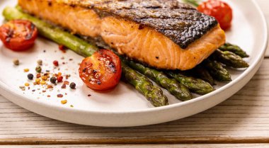 Lezzetli ızgara somon, domatesli kuşkonmaz ve ahşap masada servis edilen baharatlar.