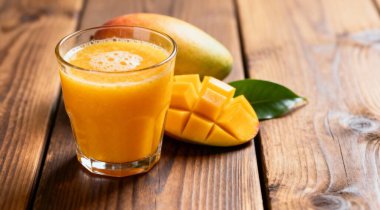 Lezzetli mango suyu bardakta taze meyve ve ahşap masa üzerinde yeşil yapraklar..