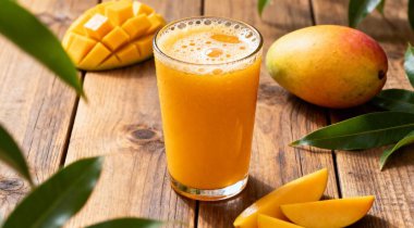 Lezzetli mango suyu bardakta taze meyve ve ahşap masa üzerinde yeşil yapraklar..