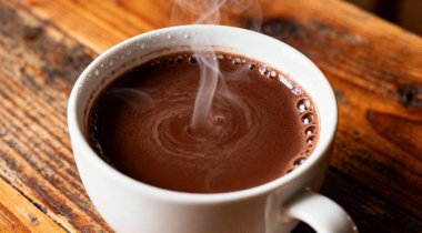 Tahta masada beyaz bir fincanda sıcak kalın çikolata.