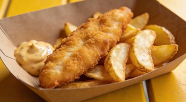 Lezzetli balık ve patates kızartması. Lezzetli sos. Sarı masanın üstünde kağıt kutuda.