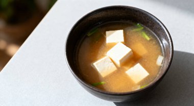 Bir kase lezzetli miso çorbası ve açık gri masada tofu, üst manzara..
