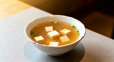Bir kase lezzetli miso çorbası ve açık gri masada tofu, üst manzara..