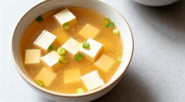 Bir kase lezzetli miso çorbası ve açık gri masada tofu, üst manzara..