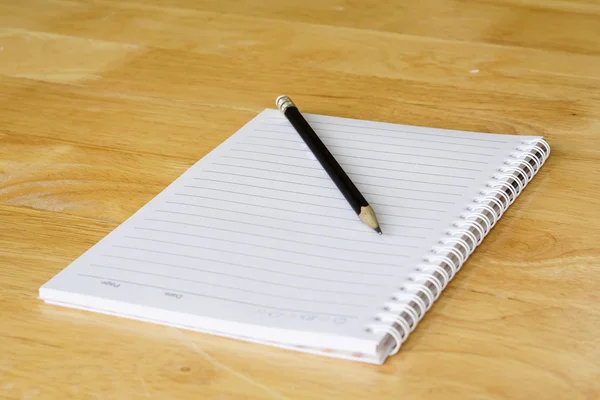 Lápis com papel e livro sobre mesa de madeira — Fotografia de Stock