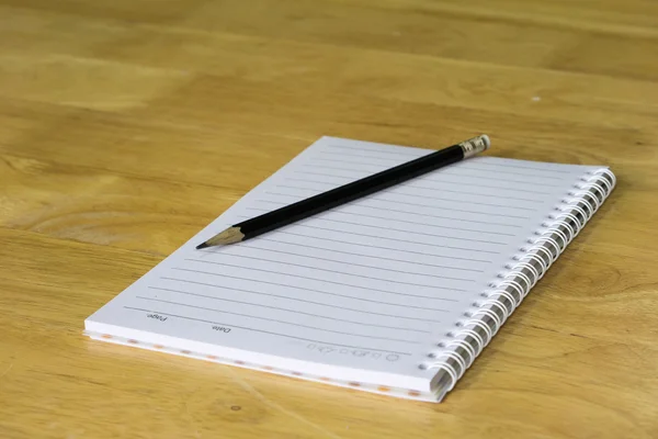 Lápis com papel e livro sobre mesa de madeira — Fotografia de Stock