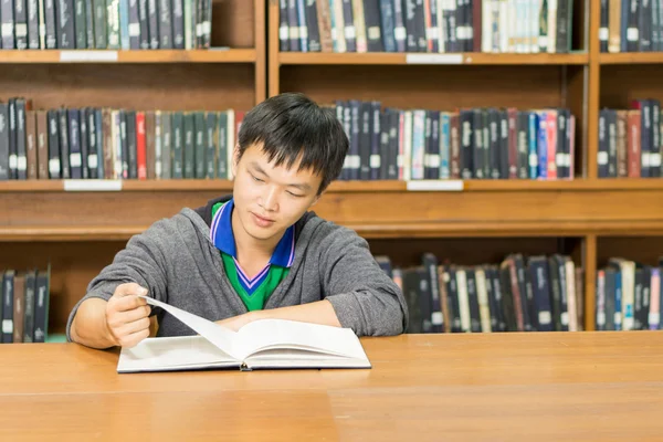 Portret van een serieuze jonge student lezen van een boek in een bibliotheek — Stockfoto