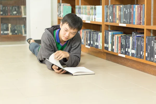 Retrato de um jovem estudante sério lendo um livro em uma biblioteca — Fotografia de Stock