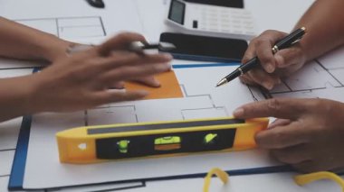 Mimarlar takımı, mühendisler mimari planları gözden geçirmek için birlikte çalışıyorlar. Planları inceliyor, bina planlarını not alıyor. Ofis ortamında olması muhtemel. Tasarım projesi için işbirliği anahtarı. Resim