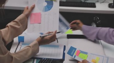 Genç iş kadını masadaki çizelgeleri ve grafikleri analiz ediyor.