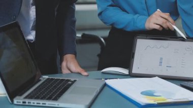İş ekibi masadaki dizüstü bilgisayar ve grafikle çalışır.
