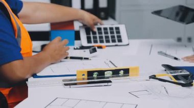 Mimarlar takımı, mühendisler mimari planları gözden geçirmek için birlikte çalışıyorlar. Planları inceliyor, bina planlarını not alıyor. Ofis ortamında olması muhtemel. Tasarım projesi için işbirliği anahtarı. Resim