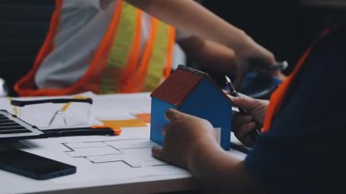 Mimarlar takımı, mühendisler mimari planları gözden geçirmek için birlikte çalışıyorlar. Planları inceliyor, bina planlarını not alıyor. Ofis ortamında olması muhtemel. Tasarım projesi için işbirliği anahtarı. Resim