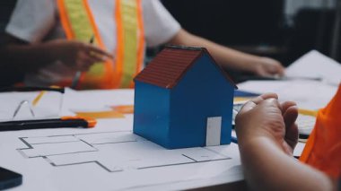 Mimarlar takımı, mühendisler mimari planları gözden geçirmek için birlikte çalışıyorlar. Planları inceliyor, bina planlarını not alıyor. Ofis ortamında olması muhtemel. Tasarım projesi için işbirliği anahtarı. Resim