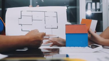 Mimarlar takımı, mühendisler mimari planları gözden geçirmek için birlikte çalışıyorlar. Planları inceliyor, bina planlarını not alıyor. Ofis ortamında olması muhtemel. Tasarım projesi için işbirliği anahtarı. Resim