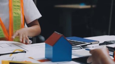 Mimarlar takımı, mühendisler mimari planları gözden geçirmek için birlikte çalışıyorlar. Planları inceliyor, bina planlarını not alıyor. Ofis ortamında olması muhtemel. Tasarım projesi için işbirliği anahtarı. Resim