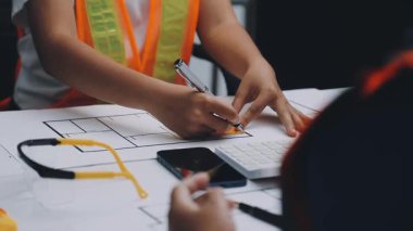 Mimarlar takımı, mühendisler mimari planları gözden geçirmek için birlikte çalışıyorlar. Planları inceliyor, bina planlarını not alıyor. Ofis ortamında olması muhtemel. Tasarım projesi için işbirliği anahtarı. Resim