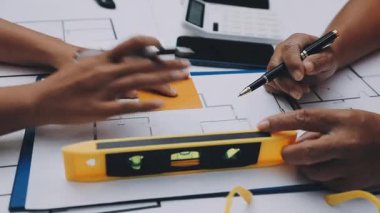 Mimarlar takımı, mühendisler mimari planları gözden geçirmek için birlikte çalışıyorlar. Planları inceliyor, bina planlarını not alıyor. Ofis ortamında olması muhtemel. Tasarım projesi için işbirliği anahtarı. Resim