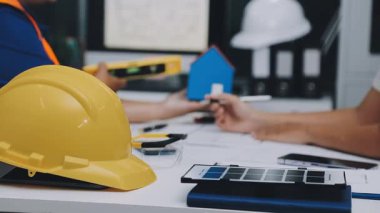 Mimarlar takımı, mühendisler mimari planları gözden geçirmek için birlikte çalışıyorlar. Planları inceliyor, bina planlarını not alıyor. Ofis ortamında olması muhtemel. Tasarım projesi için işbirliği anahtarı. Resim