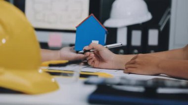 Mimarlar takımı, mühendisler mimari planları gözden geçirmek için birlikte çalışıyorlar. Planları inceliyor, bina planlarını not alıyor. Ofis ortamında olması muhtemel. Tasarım projesi için işbirliği anahtarı. Resim