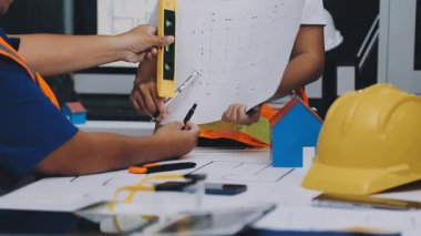 Mimarlar takımı, mühendisler mimari planları gözden geçirmek için birlikte çalışıyorlar. Planları inceliyor, bina planlarını not alıyor. Ofis ortamında olması muhtemel. Tasarım projesi için işbirliği anahtarı. Resim