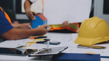 Mimarlar takımı, mühendisler mimari planları gözden geçirmek için birlikte çalışıyorlar. Planları inceliyor, bina planlarını not alıyor. Ofis ortamında olması muhtemel. Tasarım projesi için işbirliği anahtarı. Resim