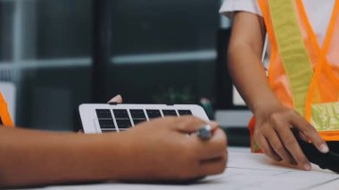 Mimarlar takımı, mühendisler mimari planları gözden geçirmek için birlikte çalışıyorlar. Planları inceliyor, bina planlarını not alıyor. Ofis ortamında olması muhtemel. Tasarım projesi için işbirliği anahtarı. Resim