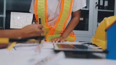 Mimarlar takımı, mühendisler mimari planları gözden geçirmek için birlikte çalışıyorlar. Planları inceliyor, bina planlarını not alıyor. Ofis ortamında olması muhtemel. Tasarım projesi için işbirliği anahtarı. Resim
