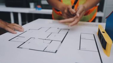 Mimarlar takımı, mühendisler mimari planları gözden geçirmek için birlikte çalışıyorlar. Planları inceliyor, bina planlarını not alıyor. Ofis ortamında olması muhtemel. Tasarım projesi için işbirliği anahtarı. Resim