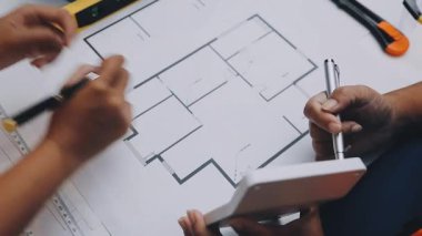 Mimarlar takımı, mühendisler mimari planları gözden geçirmek için birlikte çalışıyorlar. Planları inceliyor, bina planlarını not alıyor. Ofis ortamında olması muhtemel. Tasarım projesi için işbirliği anahtarı. Resim