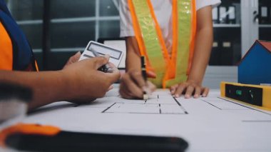 Mimarlar takımı, mühendisler mimari planları gözden geçirmek için birlikte çalışıyorlar. Planları inceliyor, bina planlarını not alıyor. Ofis ortamında olması muhtemel. Tasarım projesi için işbirliği anahtarı. Resim