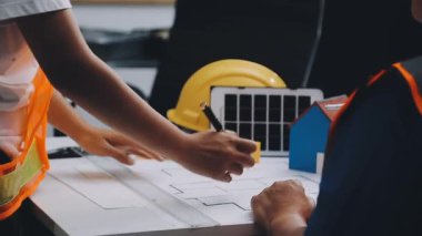 Mimarlar takımı, mühendisler mimari planları gözden geçirmek için birlikte çalışıyorlar. Planları inceliyor, bina planlarını not alıyor. Ofis ortamında olması muhtemel. Tasarım projesi için işbirliği anahtarı. Resim