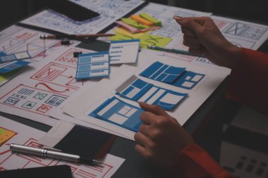 Uxui tasarımcılarından oluşan bir ekip bilgisayar ekranını işaret ederek ofiste yeni mobil uygulama tasarımını tartışıyor.