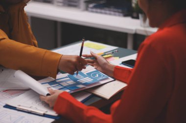 Uxui tasarımcılarından oluşan bir ekip bilgisayar ekranını işaret ederek ofiste yeni mobil uygulama tasarımını tartışıyor.