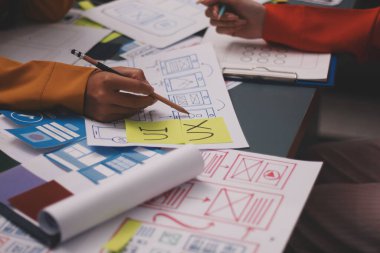 Uxui tasarımcılarından oluşan bir ekip bilgisayar ekranını işaret ederek ofiste yeni mobil uygulama tasarımını tartışıyor.