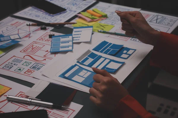 Uxui tasarımcılarından oluşan bir ekip bilgisayar ekranını işaret ederek ofiste yeni mobil uygulama tasarımını tartışıyor.