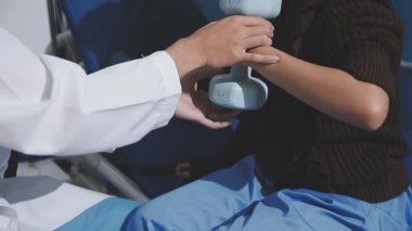 Evde dambıl kullanarak fizyoterapist eğitimi alan yaşlı bir kadın. Terapist, huzurevi egzersizlerinde yaşlı kadına yardım ediyor. Yaşlı bir hasta kollarını uzatmış halterler kullanıyor..