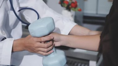 Evde dambıl kullanarak fizyoterapist eğitimi alan yaşlı bir kadın. Terapist, huzurevi egzersizlerinde yaşlı kadına yardım ediyor. Yaşlı bir hasta kollarını uzatmış halterler kullanıyor..