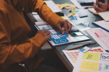 Uxui tasarımcılarından oluşan bir ekip bilgisayar ekranını işaret ederek ofiste yeni mobil uygulama tasarımını tartışıyor.