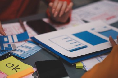 Uxui tasarımcılarından oluşan bir ekip bilgisayar ekranını işaret ederek ofiste yeni mobil uygulama tasarımını tartışıyor.