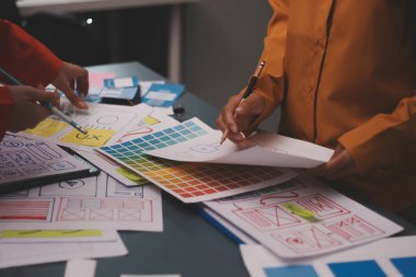 Uxui tasarımcılarından oluşan bir ekip bilgisayar ekranını işaret ederek ofiste yeni mobil uygulama tasarımını tartışıyor.