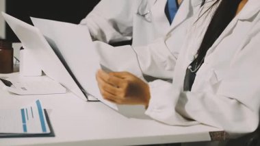Medical team meeting analyzing blood test results in hospital laboratory. Doctors and scientists in lab coats are having a discussion about blood test result, holding test tubes and taking notes.
